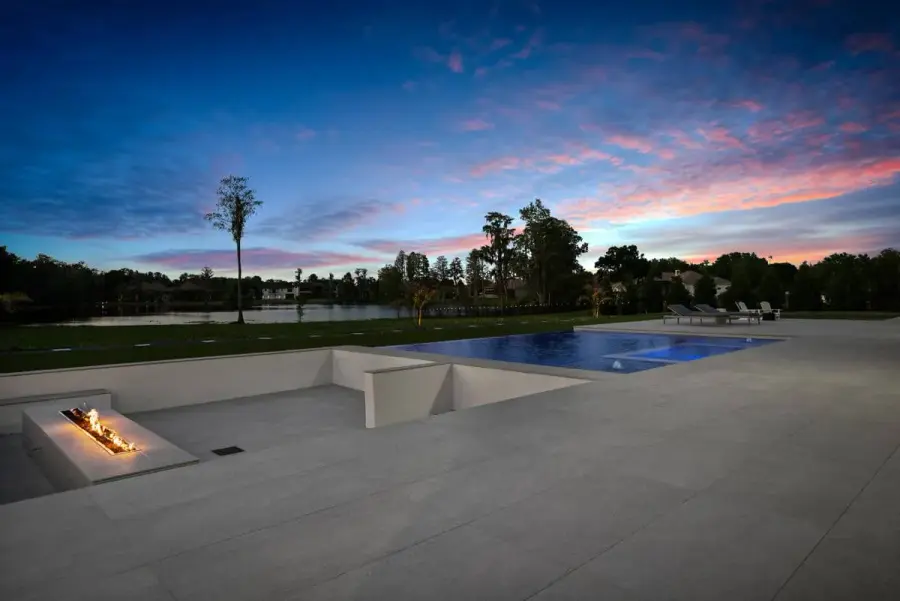 A backyard pool reflecting a vibrant sunset, with surrounding white tiles and lush landscaping completing the scene.