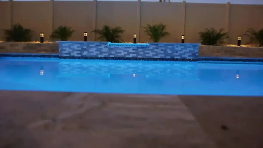 A backyard pool with a stylish water feature and well-lit landscaping, highlighting a polished tile pool deck.