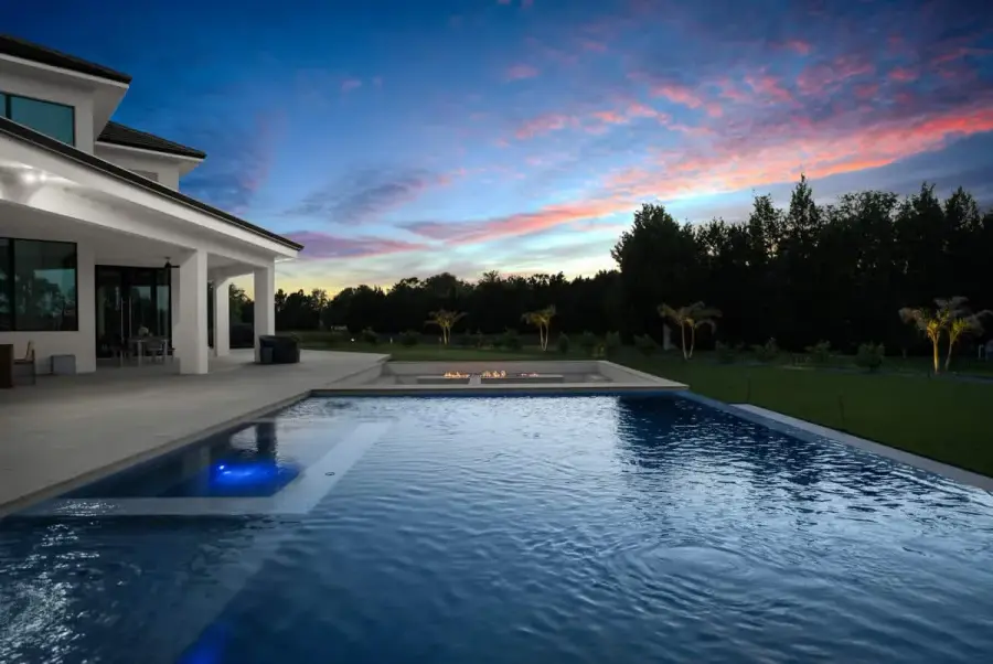 A beautiful pool reflecting a twilight sky with pink and purple hues, surrounded by contemporary architecture and trees.