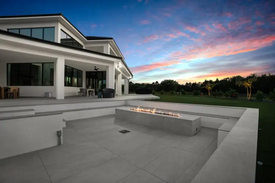 A luxurious backyard pool at dusk, with the calm water reflecting a vibrant sunset and surrounded by modern landscaping.