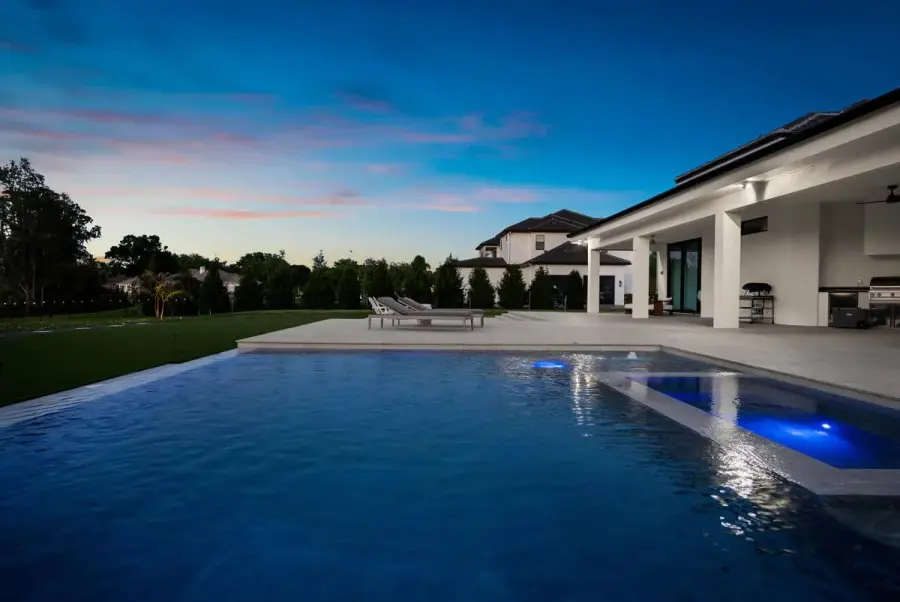 A luxurious backyard pool reflecting the sunset, with the surrounding landscape and modern architecture bathed in soft evening light.