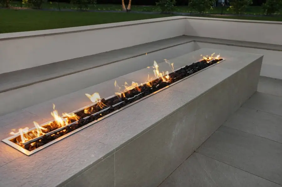 A modern fire feature with flames flickering along a smooth concrete base, surrounded by sleek backyard landscaping.