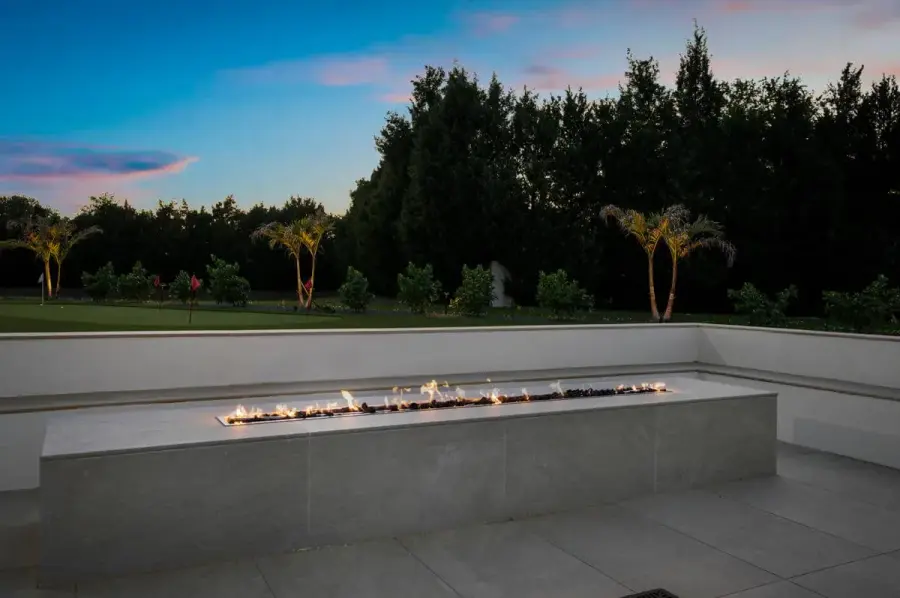 A panoramic view of a modern fire feature surrounded by trees with an expansive sunset sky overhead.