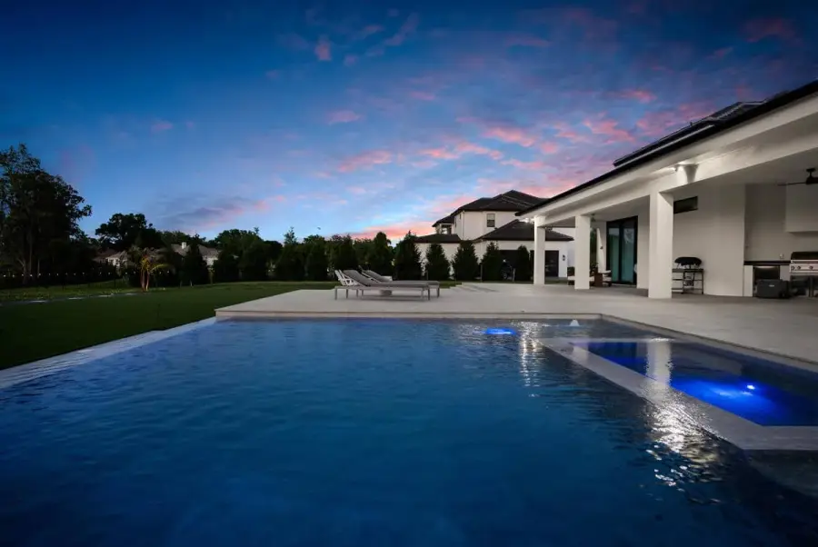 A twilight scene with a modern backyard pool, bathed in warm light from surrounding architecture and lush greenery.