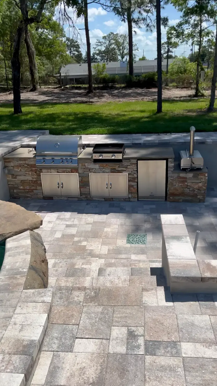 Outdoor kitchen with stone veneer, built-in grill and griddle beside a pool