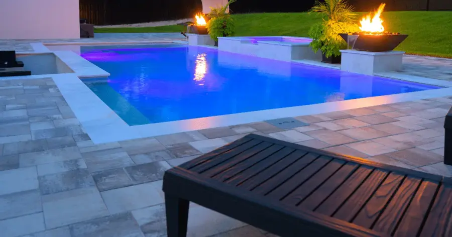Pool at dusk lit in purple LED with two fire bowls burning