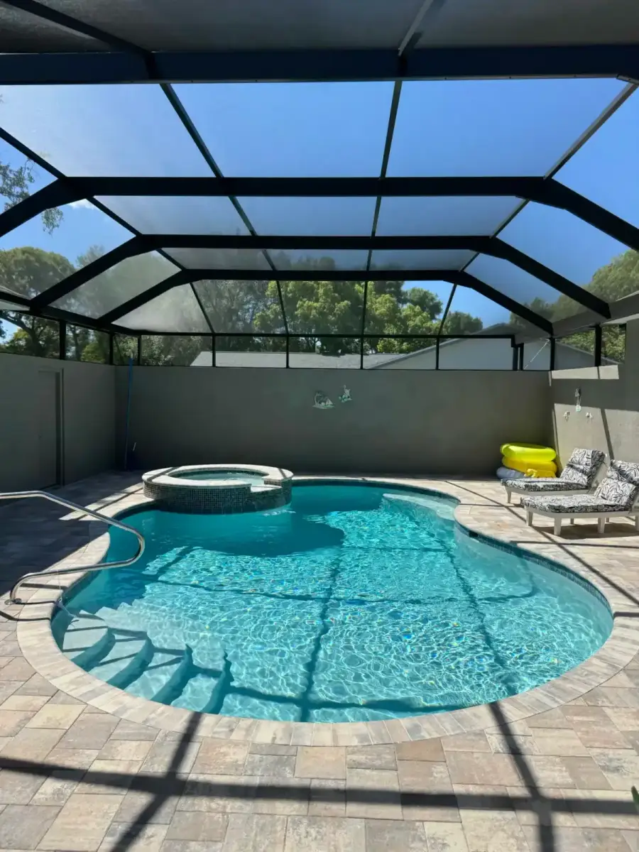 Free-form pool with a round spillover spa under a screen enclosure