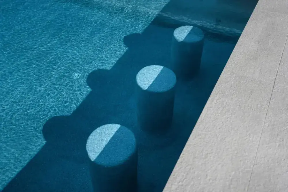 A close-up of a turquoise pool with submerged circular seating, capturing the sparkle of sunlight on water.