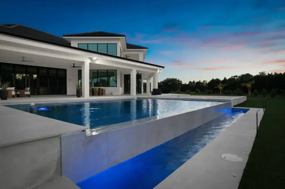 A modern backyard pool reflecting the soft colors of dusk, with surrounding contemporary landscaping.