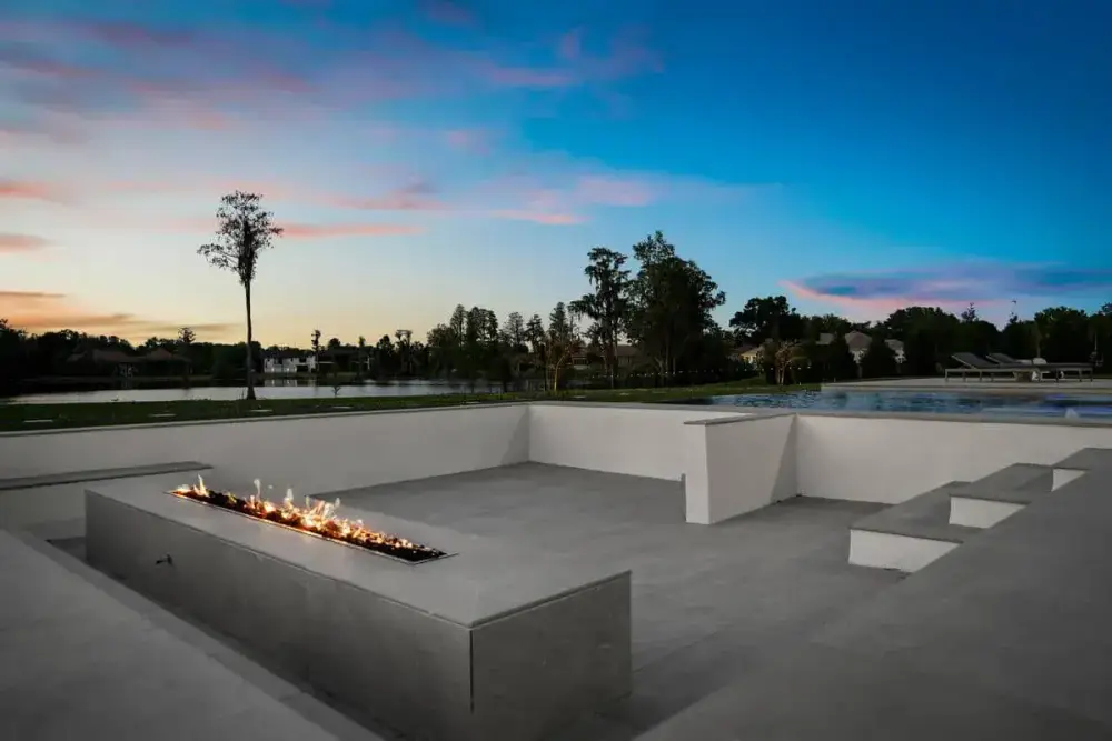 An inviting fire pit with gentle flames and contemporary outdoor seating, set against a backdrop of trees and open sky.