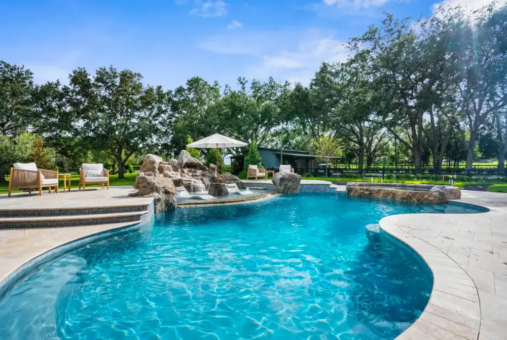 Sweeping curved pool with integrated spa, natural stone accents, and elegant landscaping in a serene backyard setting.