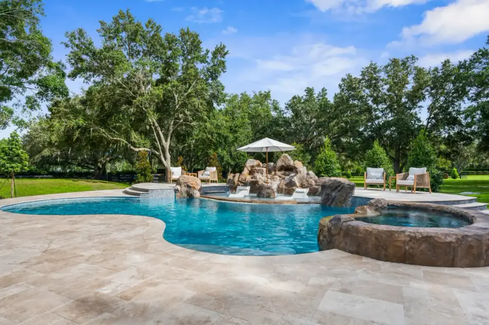 Full view of a high-end backyard pool featuring a raised spa surrounded by natural landscaping and paver decking.