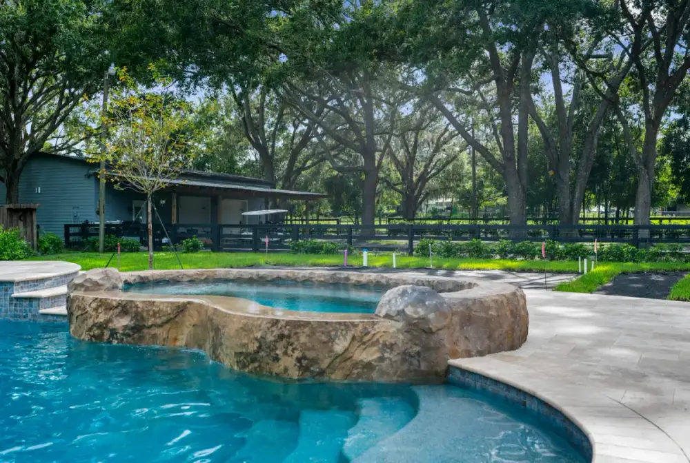 Natural rock spa with a gentle waterfall spillover into the pool, backed by mature trees and a shaded backyard retreat.